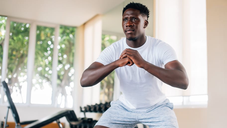 An African American man in a white shirt doing squats in his home gym